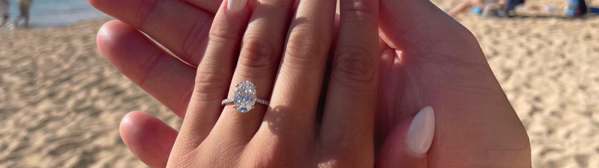 Holding hands on the beach with a diamond engagement ring.